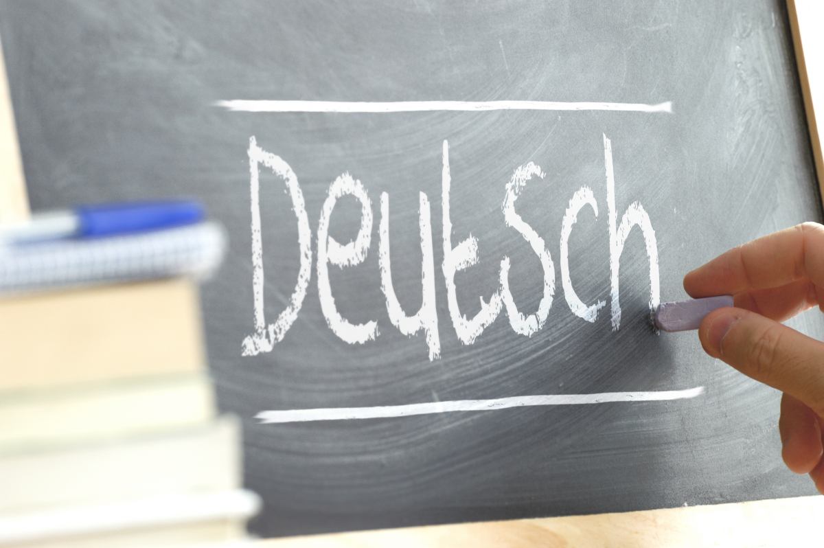 Hand schreibt mit Kreide das Wort „Deutsch“ auf eine Tafel