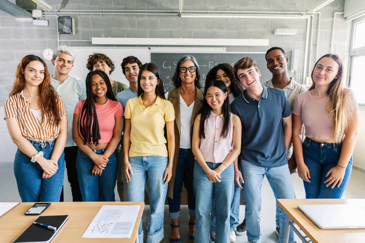 Gruppe lächelnder Schülerinnen und Schüler mit ihrer Lehrerin in einem Klassenzimmer.