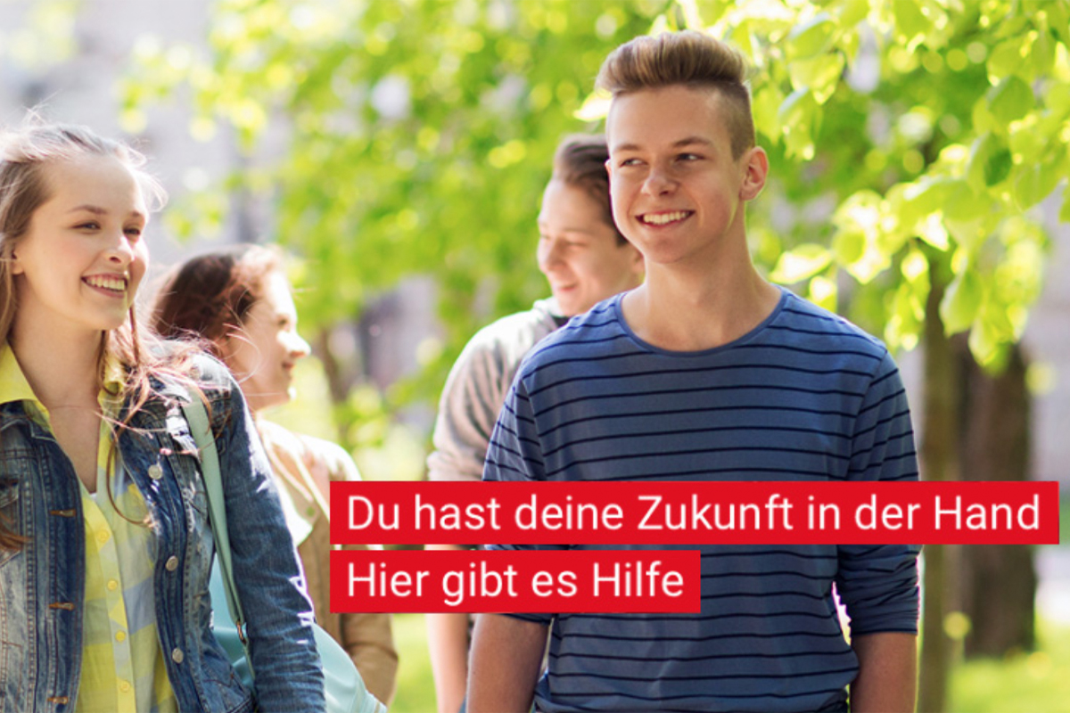 Das Bild zeigt eine Gruppe Jugendlicher, die bei sonnigem Wetter im Freien unterwegs sind. Im Vordergrund sieht man einen lächelnden Jungen in einem blau-gestreiften T-Shirt, daneben ein ebenso fröhliches Mädchen mit langer, hellbrauner Haarpracht, Jeansjacke und Rucksack. Im Hintergrund sind weitere Jugendliche zu erkennen. Die Stimmung ist freundlich und optimistisch. Über dem Bild befindet sich ein roter Textblock mit weißer Schrift, auf dem steht: „Du hast deine Zukunft in der Hand. Hier gibt es Hilfe.“ Das Bild vermittelt Zuversicht und richtet sich an junge Menschen am Übergang von Schule zu Beruf.